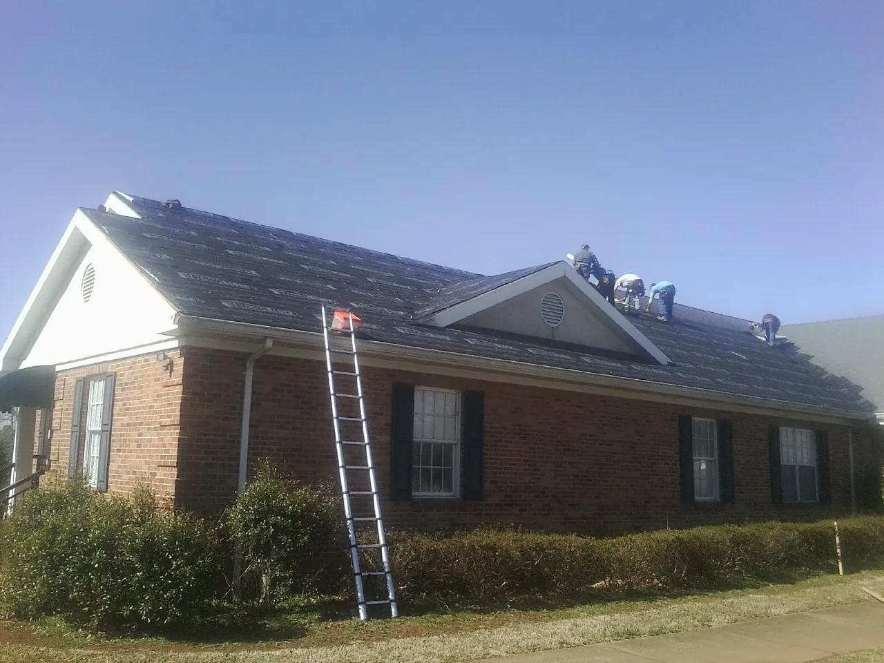 Crew tearing shingles off a brick ranch roof with a ladder set — Metal Roof Repair work by our crew in Mount Carmel