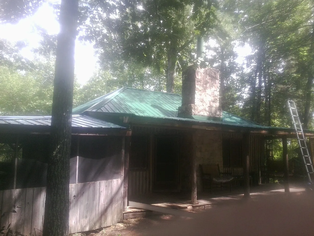 Green metal roof and stone chimney above a log cabin porch in Mount Carmel